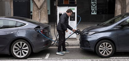 Un hombre carga un coche eléctrico en una calle de Barcelona. 
